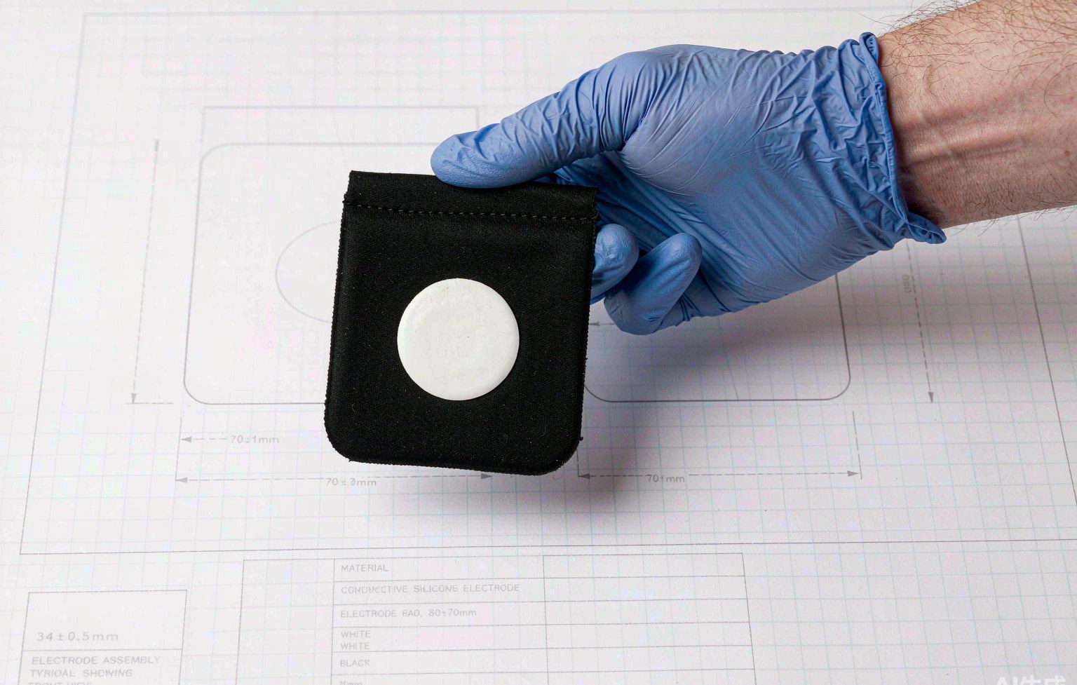 Gloved hand holding a custom electrode over technical drawings